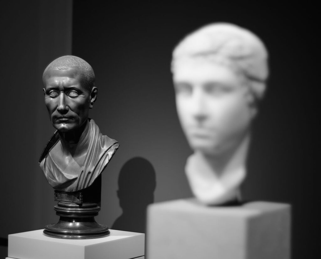 A black marble bust of Julius Caesar seemingly looking at a white warble bust of Cleopatra.