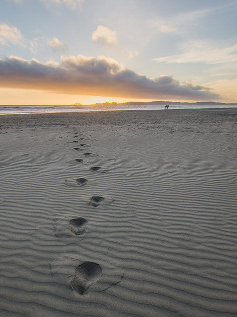 Footsteps on a beach towards the sea and the setting sun to illustrate distance.